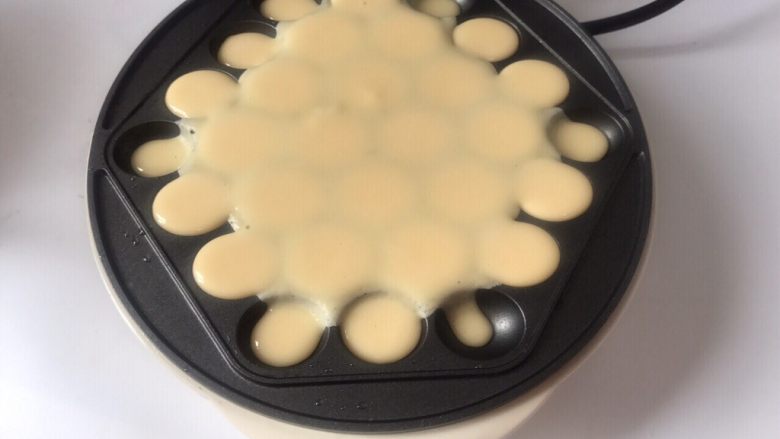 香港名小吃鸡蛋仔,倒入适量面糊,中间厚一点,边上少一点,免得溢出来,盖上盖子,戴上防烫手套将机器翻面倒立1分钟左右再翻回正面