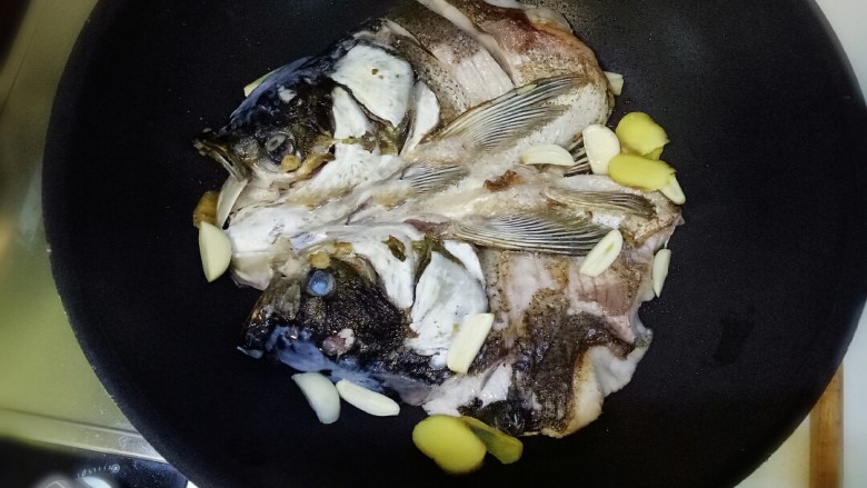 鱼头炖豆果,煎至表皮金黄翻个面,煎一会放生姜大蒜爆香下