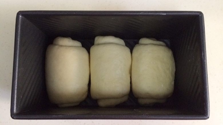 炼乳吐司(中种法),把卷好的面团依次放入吐司盒内。