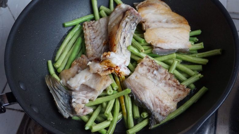 豆角焖鱼,将豆角翻到锅底,鱼肉放在豆角上面。
