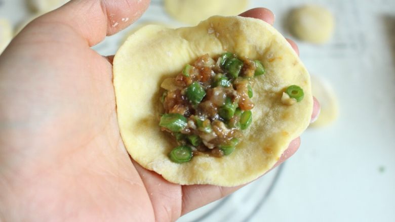 豆角猪肉生煎包,剂子按扁之后擀圆。将包子皮放在手心里,放入一勺肉馅,
