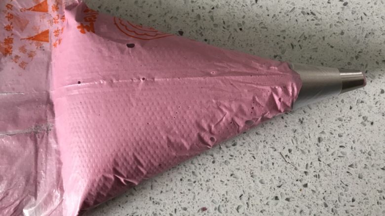 小粉马,将面糊装入裱花袋,用刮板将面糊推到裱花袋前端。这步就要开始预热烤箱了,有热风功能的烤箱直接开热风上下火165度,预热30分钟,因为马卡龙的最佳温度在155到165之间,她对温度特别敏感,太高会上色,太低导致马卡龙空心。一般家用普通烤箱预热在30分钟左右是最稳定的状态,所以要预热30分钟。