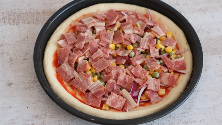 培根披萨,将配料均匀的撒在披萨饼底上。