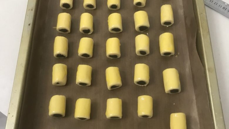 豆沙一口酥,三条全部做完排在一起切成3厘米长一段放入烤盘,表面刷上蛋黄液。