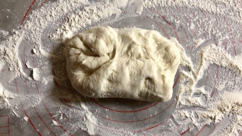 发面葱油饼,台面上撒上干粉,把面团取出,进行按压排气。