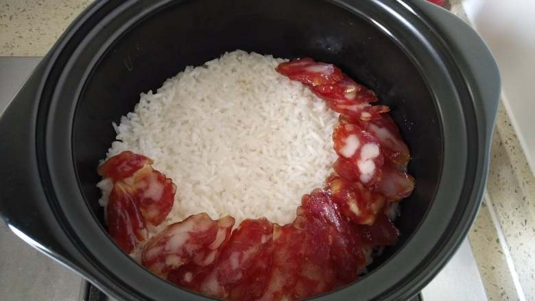 腊味煲仔饭,转小火几分钟后,开盖检查米饭状态,米饭已经吸水差不多了,基本定型了,迅速铺上切好片的腊肠。