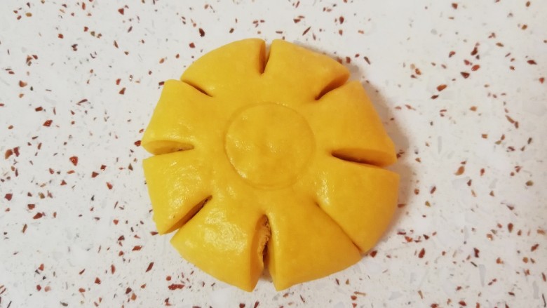 南瓜肉松花朵包,包好肉松的面团压扁,用擀面杖擀开,用中号裱花嘴在正中间压一个圆圈,用刮刀分成8等份,花朵面包胚就做好了,依次做好剩下的面包。