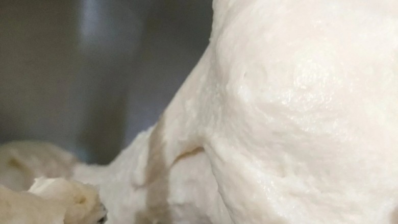 紫薯豆包,当面团逐渐变得光滑时,加入盐和切成小片的黄油。厨师机换低档,直到盐和黄油完全融入面团中后再换高速档,打出手套膜。