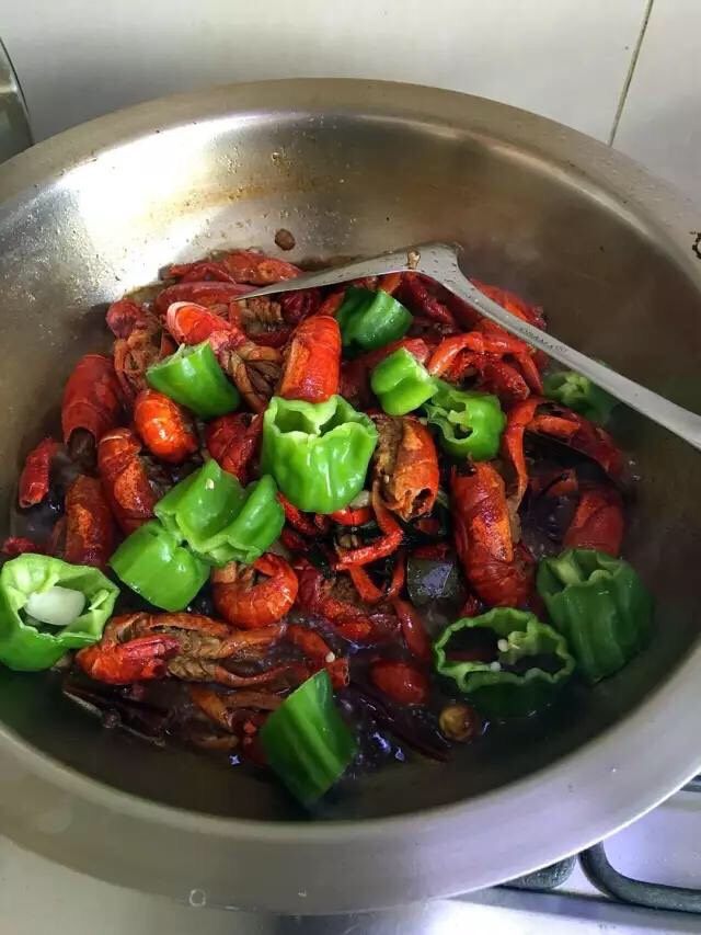 啤酒麻辣小龙虾,打开锅盖放入盐和蒜瓣,翻炒均匀后,再次盖上锅盖焖煮5分钟。5分钟以后揭开锅盖,开大火放入青椒筒。翻炒至青椒变色后,关火。