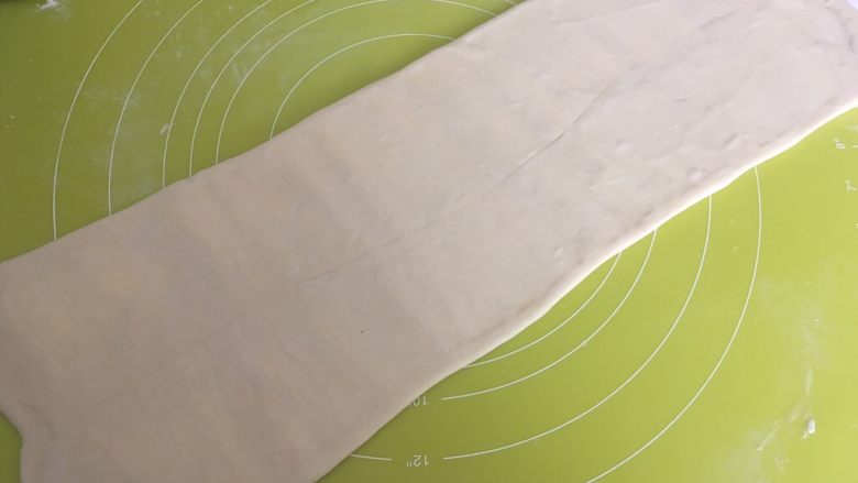 手揉可颂牛角包,揉面垫上撒点干粉,用擀面杖从中间向两边擀开,将面片擀长,长度40多厘米