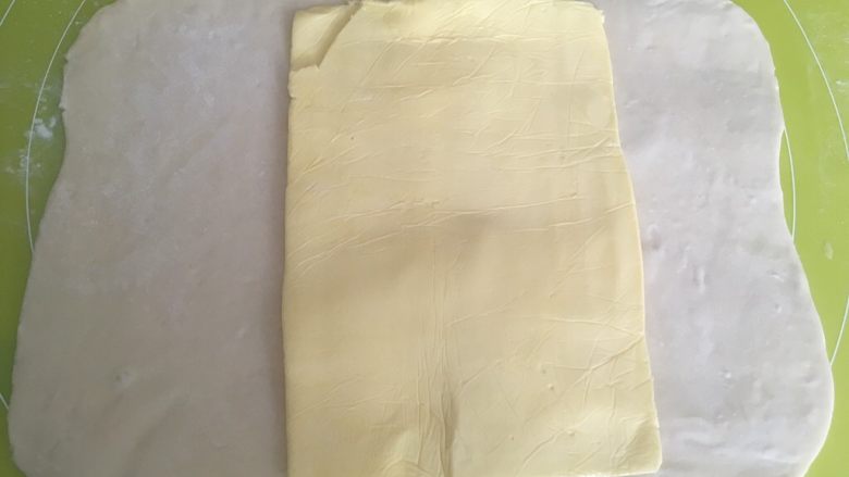 手揉可颂牛角包,取出冷冻的黄油片,用剪刀裁掉保鲜袋,将黄油铺在面片中间,一起室温回下温,面片变软,可以对折即可