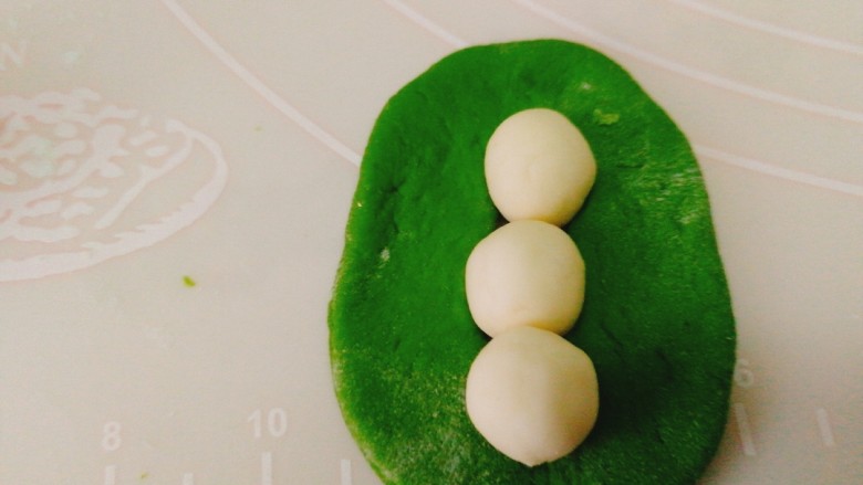 人见人爱的豌豆荚馒头,取出少量白色面团,搓小圆后放在绿色面团中间