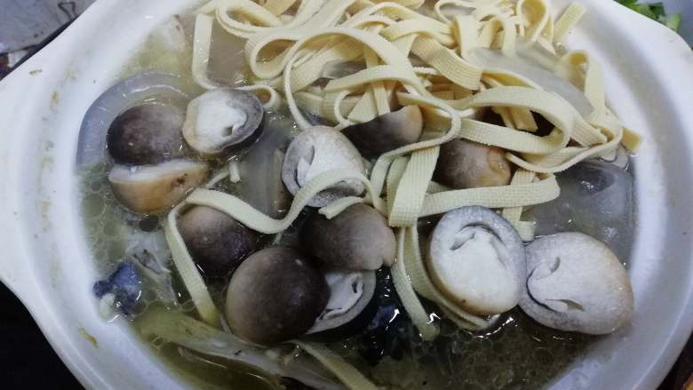 千岛湖鱼头汤,厚百叶切丝捞烫后,与粉皮和草菇一起倒入鱼头汤,开小火继续煲煮。