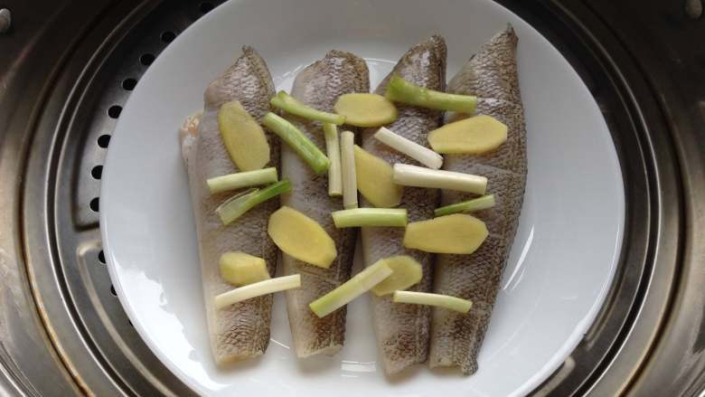 清蒸南极冰鱼,冰鱼腌好后,将香葱段和姜片均匀摆放在冰鱼上,入蒸锅,上汽后蒸8分钟