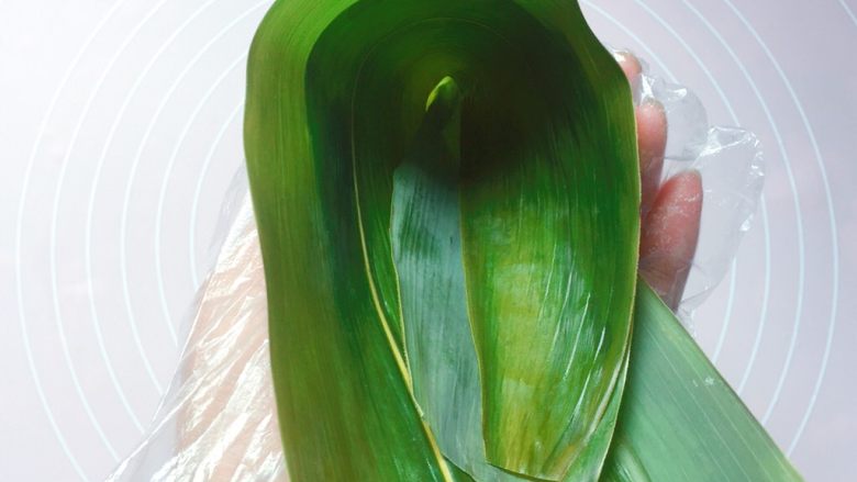 蜜枣西米粽子,在粽叶的1/3处折起,折出一个漏斗形状(漏斗下方一定要紧密,不然会漏米);