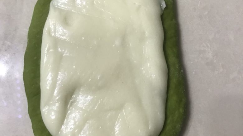 抹茶紫米麻薯软欧,取一个松弛好的面团擀成长舌形,放上麻薯,麻薯比较粘手夹放在保鲜膜上擀开再放在面皮上如图