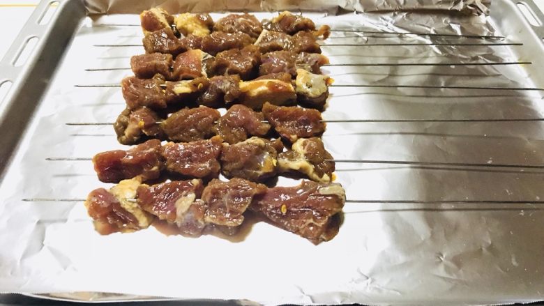 烤牛肉串,冰箱取出,将牛肉串入钢签,烤盘里铺上锡纸,摆上牛肉串,刷上一层玉米油