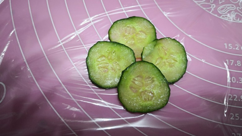 【童趣早餐】,开始整花型,先铺一层保鲜膜,将火腿肠切一个圆片,放中间,作为花心,接着将准备好的黄瓜片依次摆上去,作为花瓣。