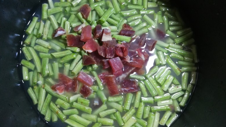 腊味豆角焖饭,再倒入咸肉粒,一定要记得不要去搅动下面的米粒,下面的米翻上来,容易夹生,煮不熟。只需要把长豇豆和咸肉粒撒在上面就好。