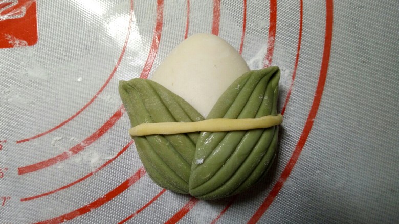 萌粽豆沙包,再取适量的黄色面团,揉成条状,环绕贴在叶子上。