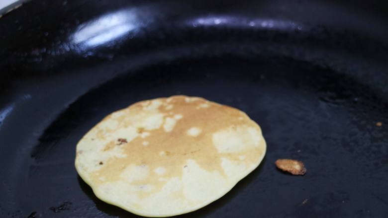 美味下午茶小点心甜糯香蕉饼,平底锅中刷一层油，用勺子取适量面糊放入平底锅中间，让面糊自动流动成圆形。一面煎制金黄后轻轻的翻一面继续继续进行煎制，