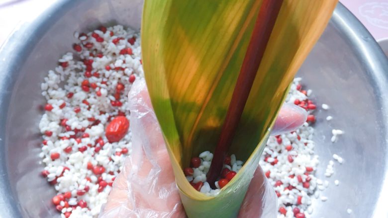 红豆红枣牛角粽,在牛角漏斗中舀入1/3的红豆、糯米,拿筷子捅实;