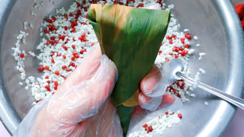 红豆红枣牛角粽,先把两边的粽叶往中间压,再把顶端的粽叶往下折;