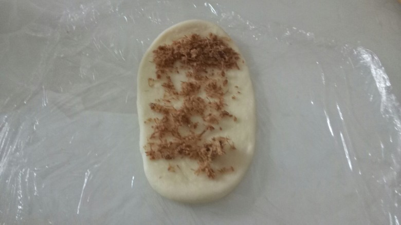 两种口味的鸡腿面包,取一个面团,用手压扁,擀成长形,上段距离0.5厘米的位置放上肉松。