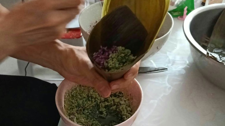 彩色果干甜粽子和咸味肉粽子,取两片粽叶一半放抹茶色糯米,一半放紫薯色糯米,中间包上一颗蜜枣和果干,再在上面放糯米。
