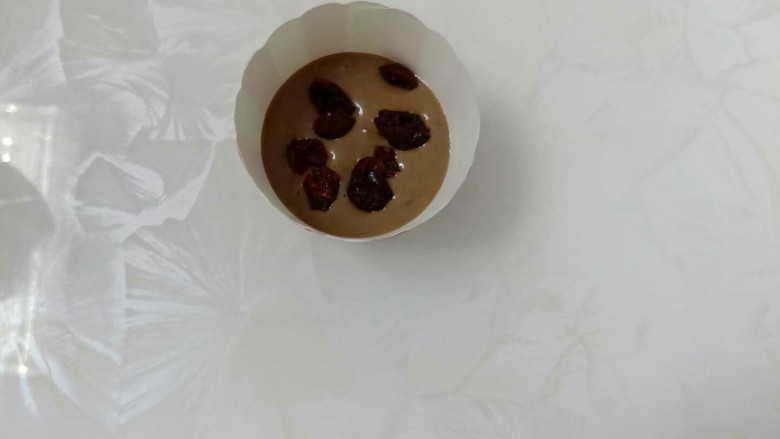 可可味蔓越莓芝麻爆炸头麦芬,倒入纸杯中1/3,撒上蔓越莓干。