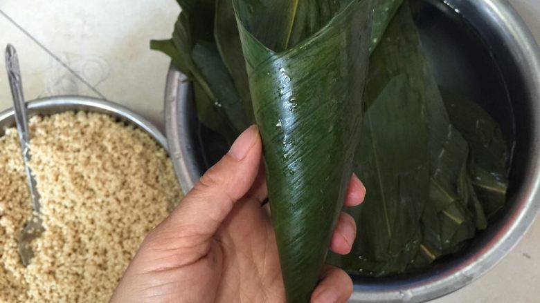香香肉粽,将两片粽叶半重叠平放,捏住叶尾部向叶头部旋转成斗型。