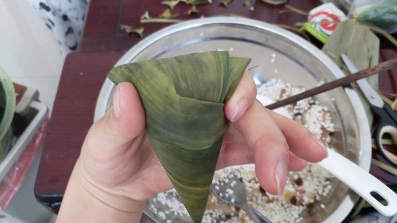 不同类型粽子的包法,把剩余的叶子向一边对折,用手固定住。