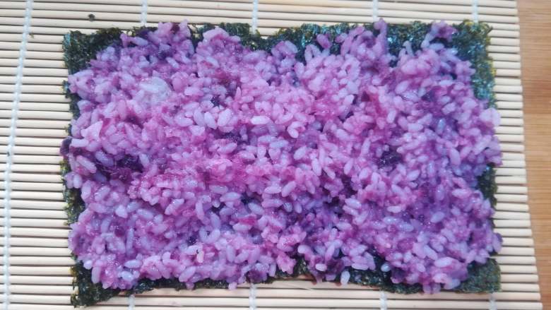 紫薯寿司,把拌匀的紫薯米饭均匀的铺在紫菜上,紫菜的两端也要有米饭粒。如果觉得米饭比较粘,可以用勺子沾水,有勺背来把米饭推均匀。用手来操作的话,也可以在手上抹些凉开水,或寿司醋防止黏手。