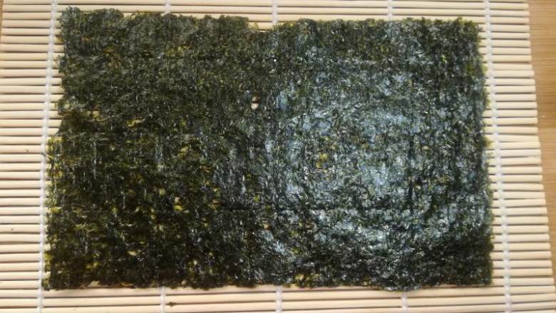 紫薯寿司,取半张海苔铺在卷帘上。今天的这种卷法只需要一次半张就够了。做寿司的紫菜是专门的<a style='color:red;display:inline-block;' href='/shicai/ 75428'>寿司海苔</a>,不是普通的紫菜哦,超市有售。