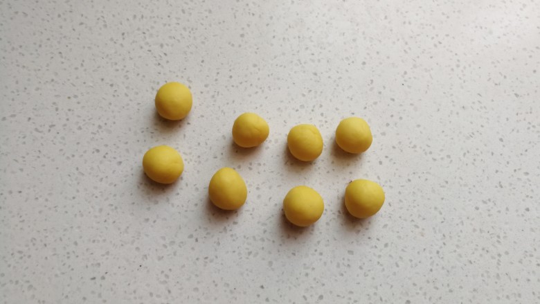 彩色风车豆沙包,黄色的小面团分成均等的八个小剂子搓圆,然后盖上保鲜膜把它放入冰箱冷藏待用。