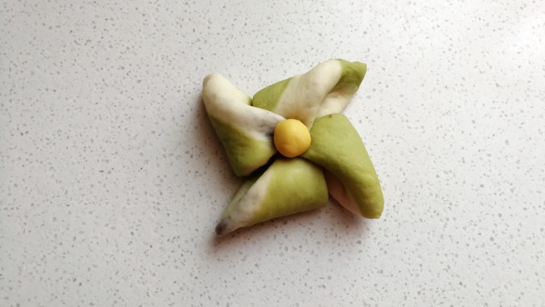 彩色风车豆沙包,叠好后用筷子在中间按压几下,然后取出先前冷藏的黄色小面团摆上去,这样一个风车面包胚就完成了。