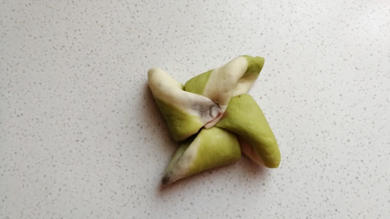 彩色风车豆沙包,再依次掀起一个角顺着一个方向朝中间折叠过去,一片叠一片压紧。