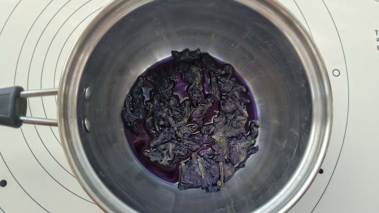 旗袍玛德琳,先将蝶豆花干花与清水放入小锅里小火加热,煮开后2分钟左右关火。用过滤网把蓝色的蝶豆花汁过滤出来30克备用。
