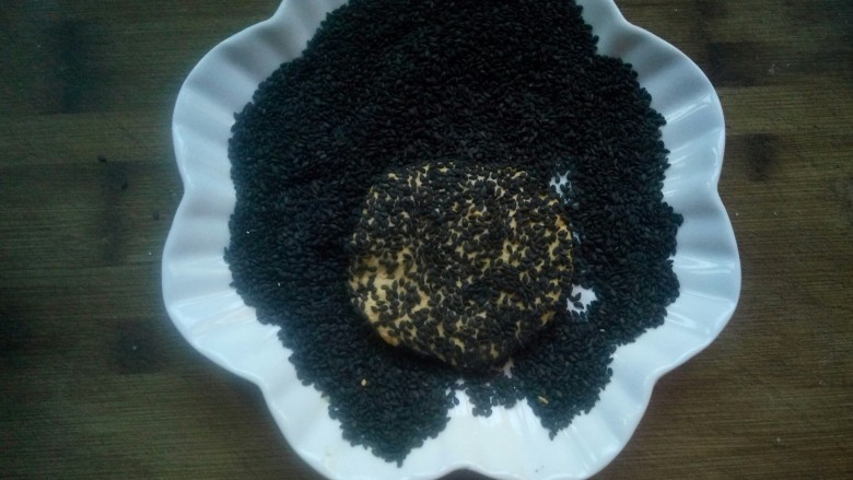芝香南瓜饼,放入盛黑芝麻的盘子里,使两面都沾满芝麻,拿出来再按压下,使其芝麻粘的更牢靠,以免入锅煎的时候,芝麻掉下来。