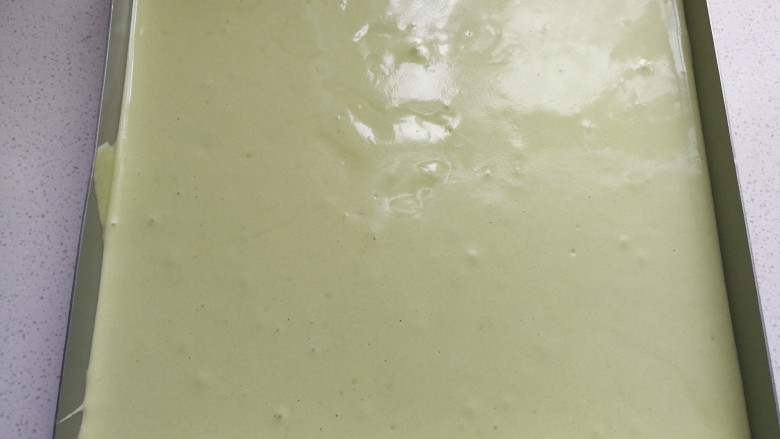 足球慕斯蛋糕卷,接着把先前拌好的抹茶蛋糊倒入烤盘中,用刮板抹平表面并轻轻震荡几下,再放入预热好的烤箱中层上下火180度烤约25分钟左右。