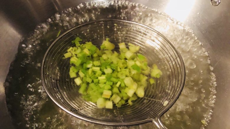 凉拌芹菜毛豆米,将芹菜粒放抄网里在热水里烫10秒钟,拿出,直接沥干水倒入调料碗里。