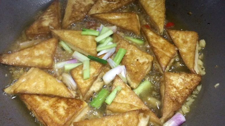超级下饭的香煎豆腐块,等水少一半左右时,放入葱梗,同时给豆腐块翻面。