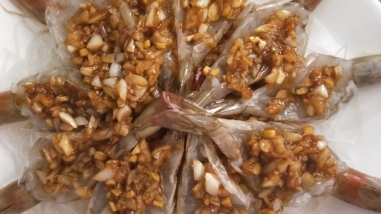 蒜蓉粉丝基尾虾,将泡发好的粉丝装入盘内,在粉丝上放入适量炒好的蒜蓉,然后摆上基尾虾再把剩下的蒜蓉放在虾背上,如图