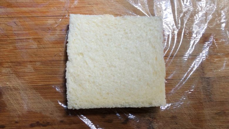 自制三明治,菜板上铺一张保鲜膜,放上一片吐司