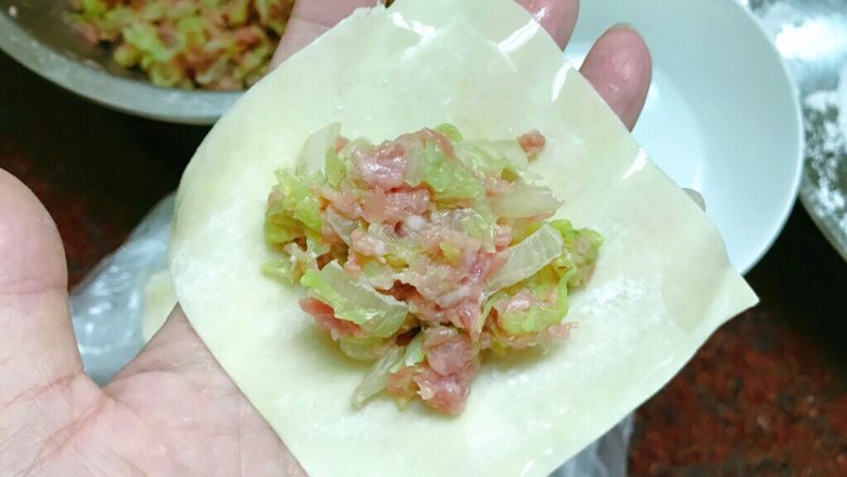 白菜肉末饺子,取一张饺皮,把馅放在中间,用水抹在皮边上。