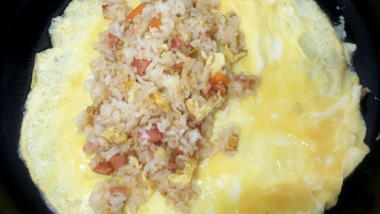 家常蛋包饭,倒入炒好的米饭,对合上蛋饼,用锅铲固定好封口。