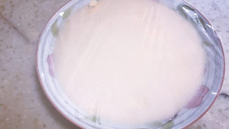 芒果双皮奶,倒入盘中,盖上一层保鲜膜,用牙签适当在膜上扎一些小孔,然后放入锅中蒸8分钟左右