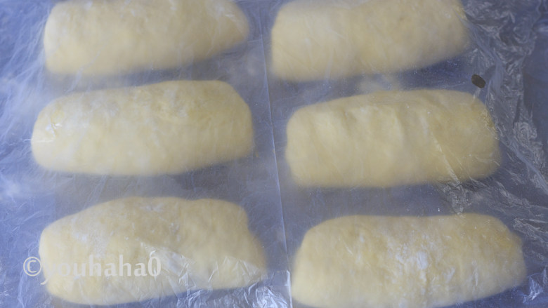 汤种牛奶吐司,醒发后的面团翻面、拍扁、上下擀开,再自上往下卷起,依次做好6个面团,继续改保鲜膜醒发15分钟左右。