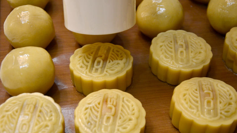 广式蛋黄莲蓉月饼 私房烘焙版本,用100克月饼模具,装好COUSS字样图案,在内腔刷一层薄花生油,先将模具扣入烤盘中的面团上,按下图案到位后松手脱模,也可按压几次后脱模。