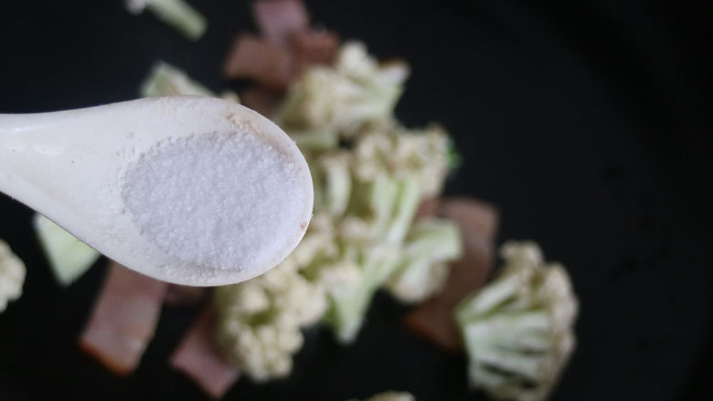 美味菜花炒培根,调入白糖、适量的盐,继续翻炒均匀。